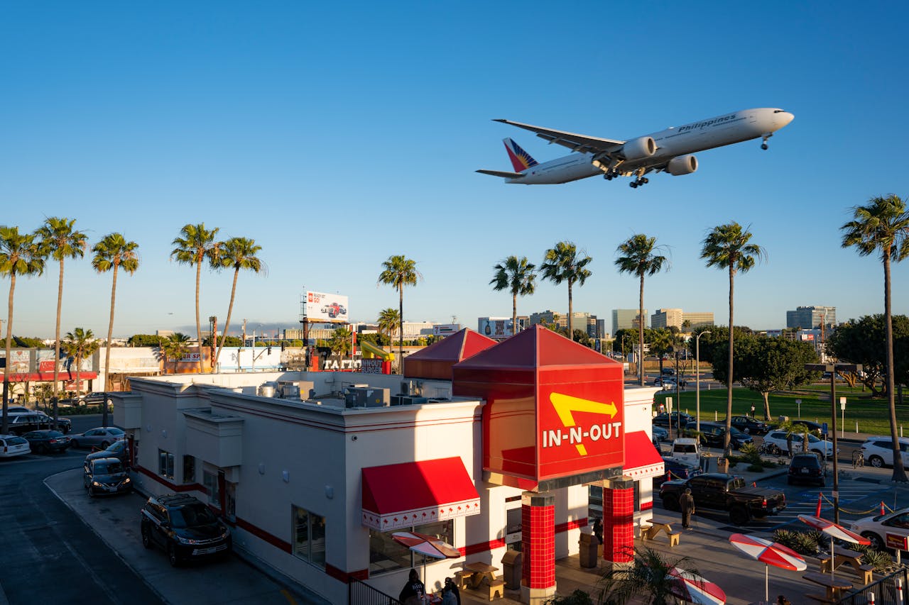 A plane flying over In-N-Out Burger with palm trees in Los Angeles, California.